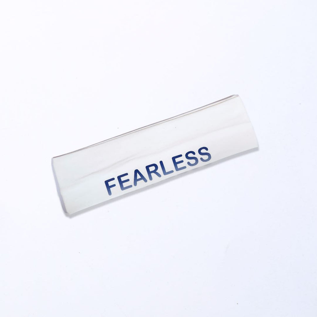 This white headband has the word "Fearless" printed on it. The headband is made of a soft, moisture-wicking fabric and features silicone for a firm hold. 