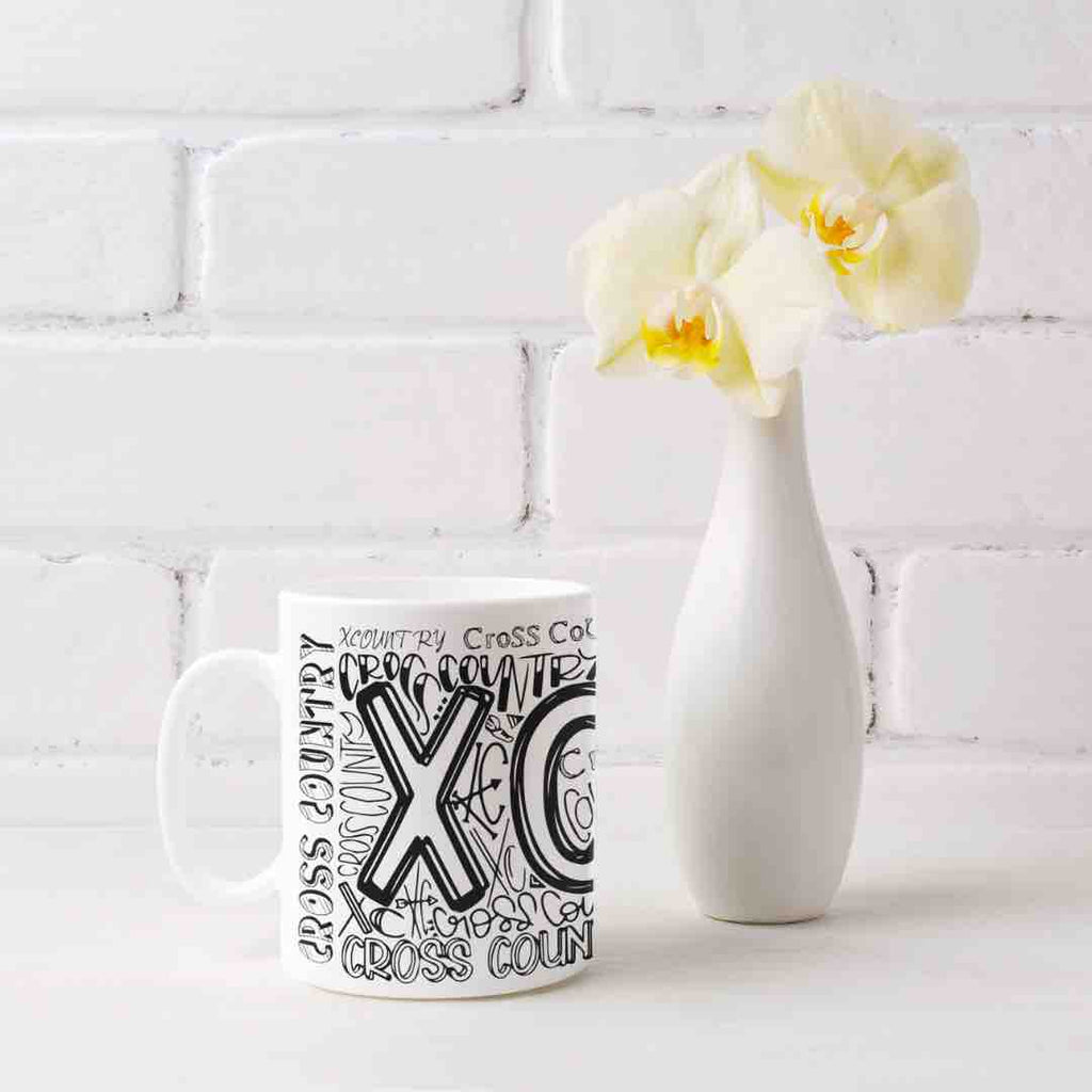 A white ceramic coffee mug with a graffiti-style design featuring the words "XC", and "CROSS COUNTRY" in bold, colorful lettering. It's microwave and dishwater friendly. 