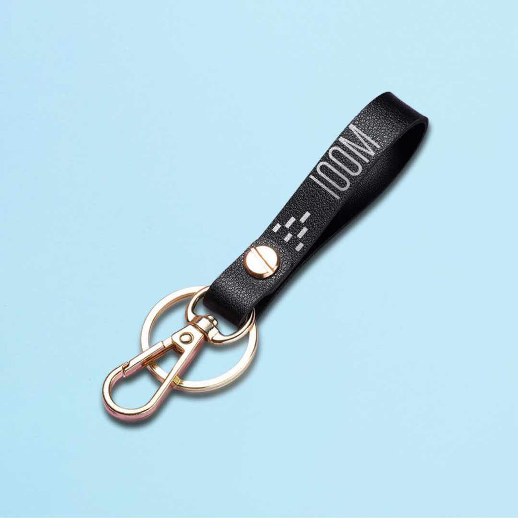 A close-up photo of a black leather keychain with the text of a 100m running track with a metal finish, a stylish and functional accessory for track and field enthusiasts