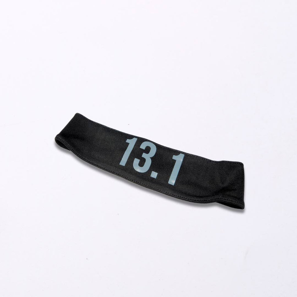 Image of a black sports headband with a bold print of "13.1" on it. The headband is made of a soft and stretchy polyester fabric with a silicone grip on the inside to prevent slipping. Ideal gift for sport enthusiasts. 