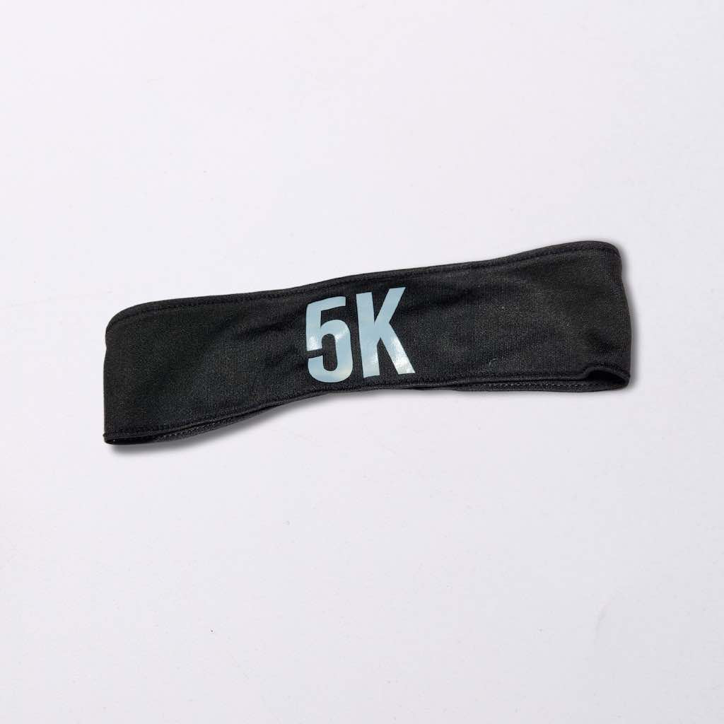 A black headband with the words ‘5k’ written on it in white. The headband is made of a soft, and stretchy material suitable for long distance and cross-country races. 