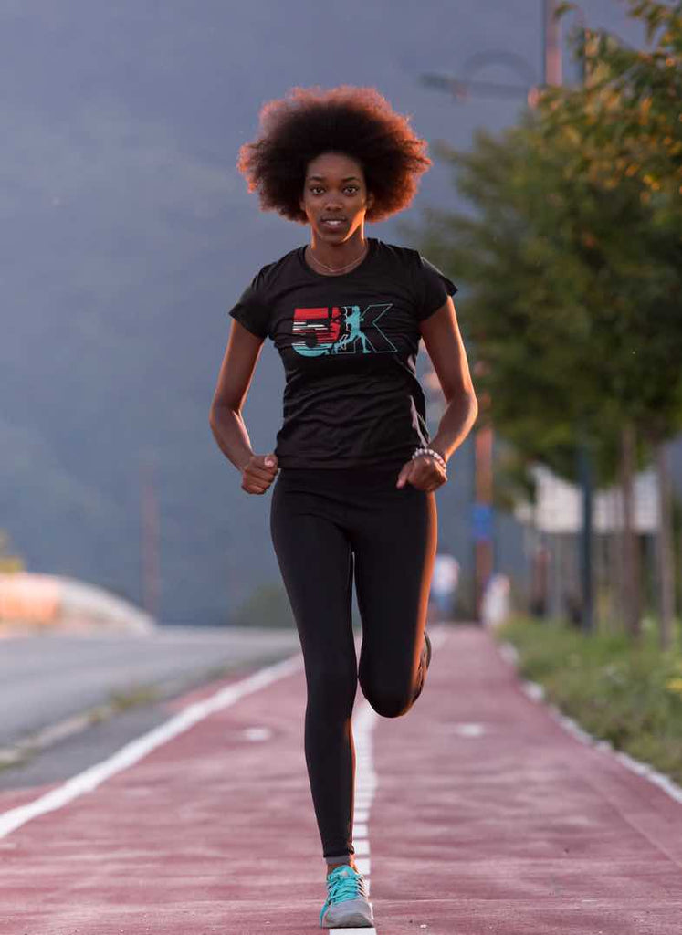 afro head woman running 5k on a running trail wearing a black running t-shirt with a 5k graphic