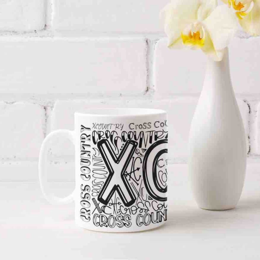 A white ceramic coffee mug with a graffiti-style design featuring the words "XC", and "CROSS COUNTRY" in bold, colorful lettering. It's microwave and dishwater friendly. 