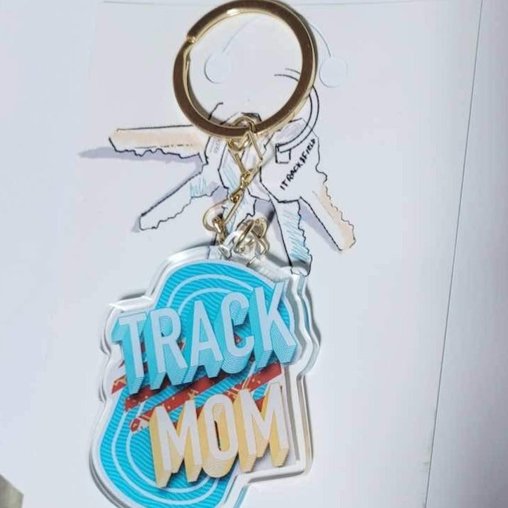 A clear acrylic keychain with a bold, red and blue and yellow design reading "Track Mom", perfect for showing support for a loved one in track and field.